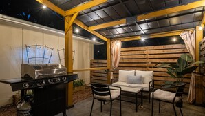 Eine Terrasse im Freien mit Grill, Sitzgelegenheiten und einer Pergola.