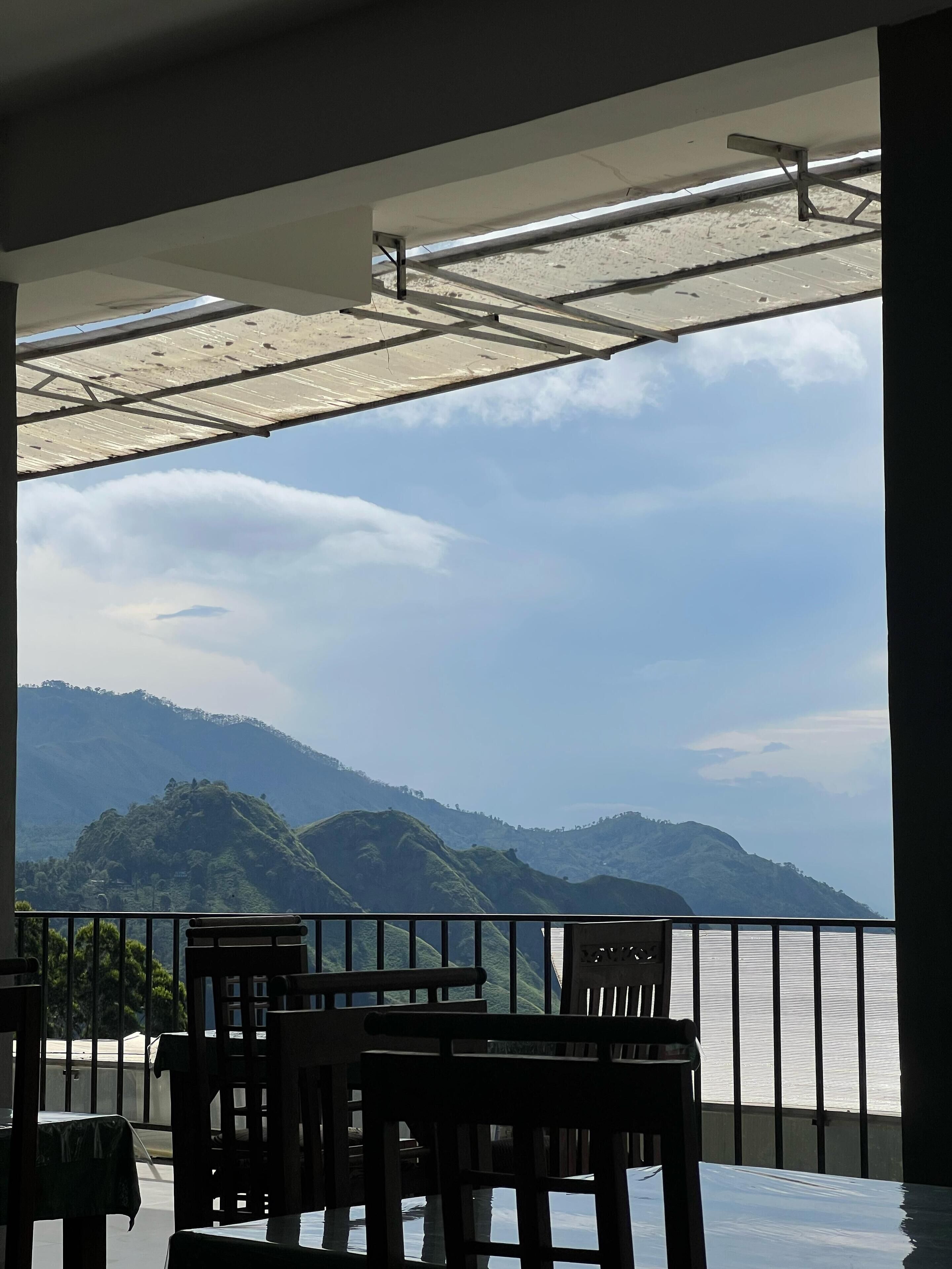 A terrace with tables and chairs, overlooking a mountainous landscape and a body of water.