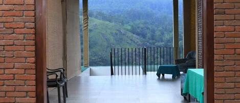 A covered outdoor area with a view of a mountainous landscape. There are chairs and a table with a green tablecloth.