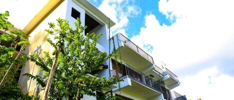 A multi-story building with balconies, surrounded by greenery.