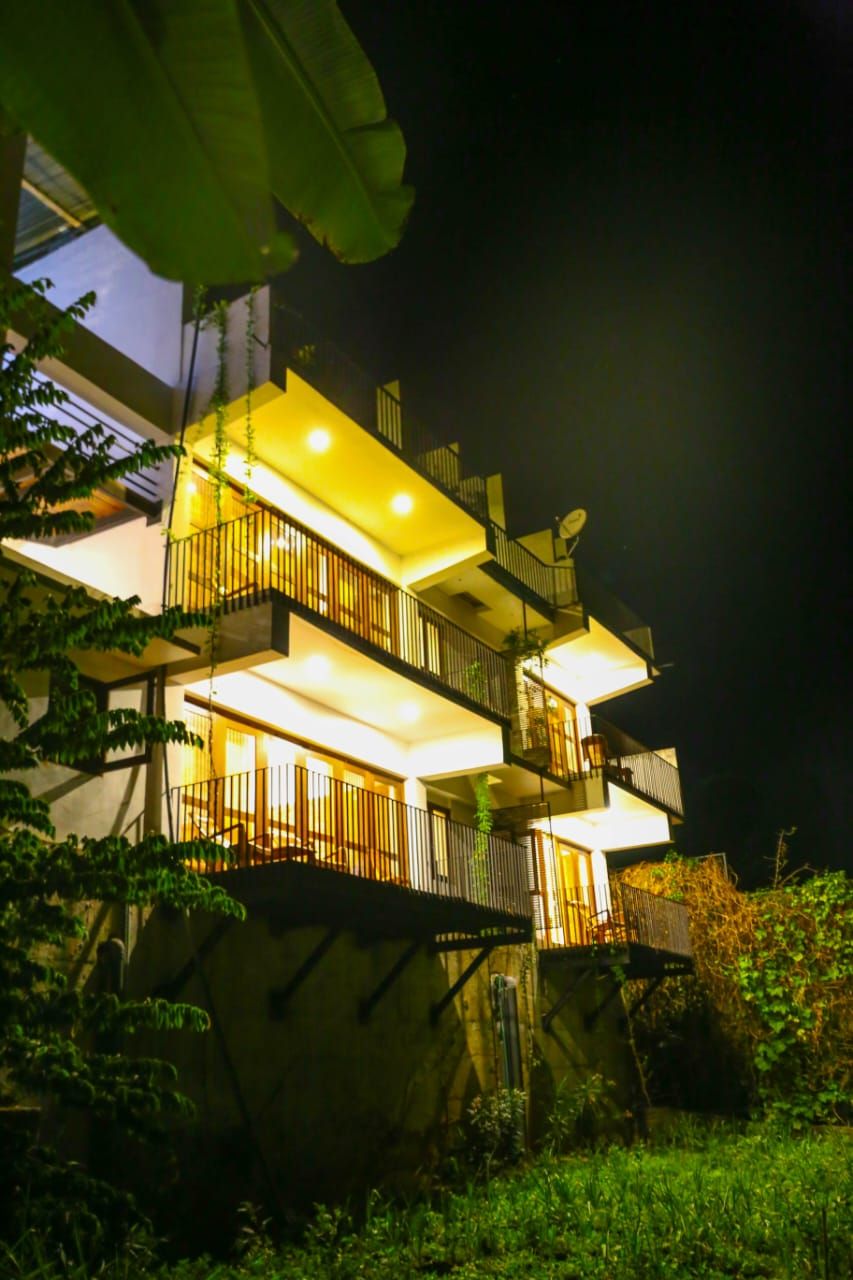 Un edificio de varios pisos con balcones, rodeado de vegetación.