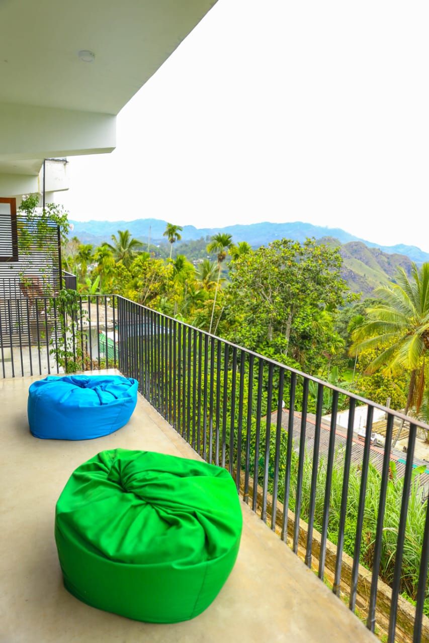 A balcony with two bean bags, a metal railing, and a view of lush greenery and mountains.