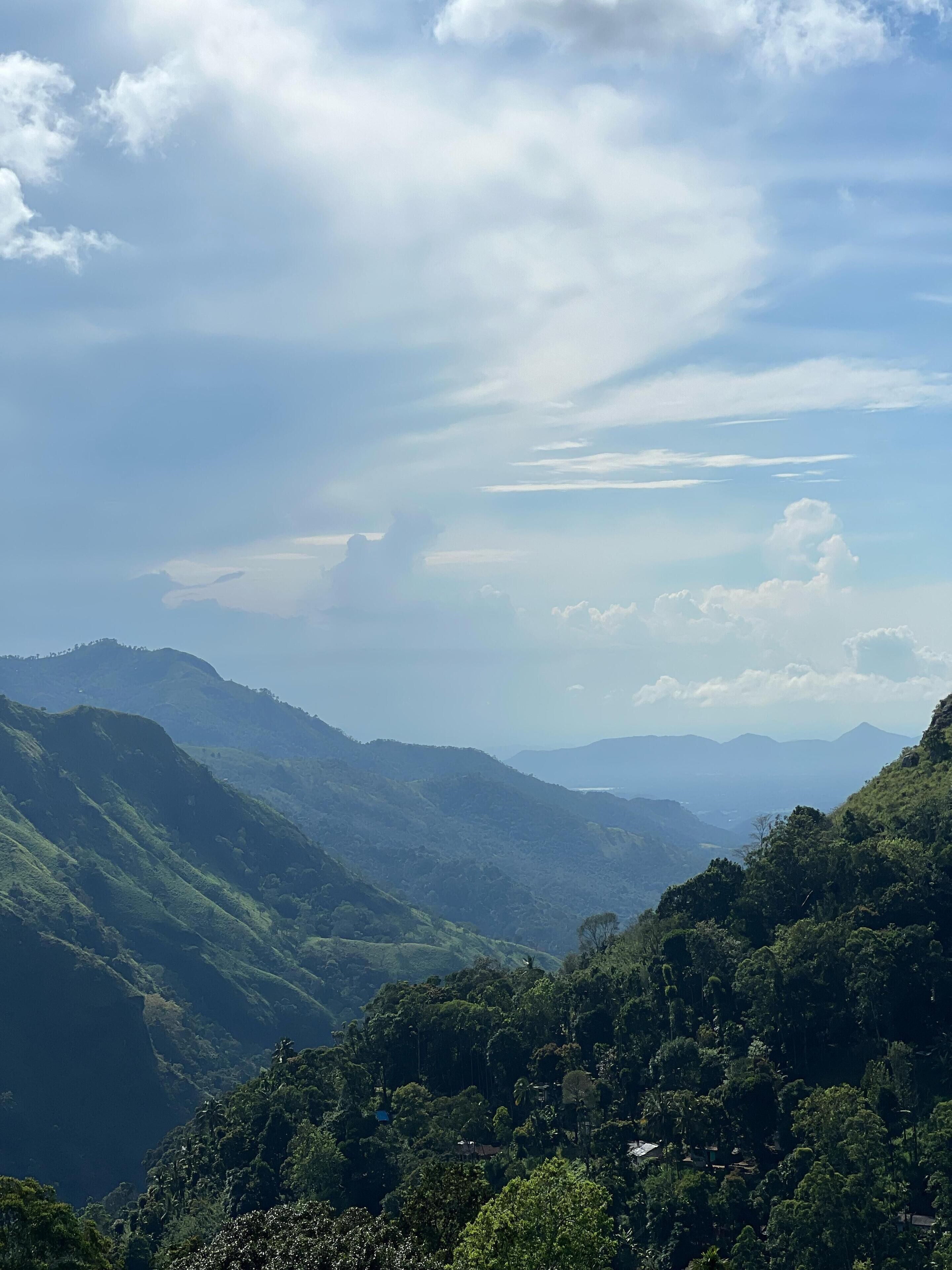 A mountainous landscape with lush greenery and distant hills under a partly cloudy sky.