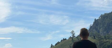 A man standing on a balcony overlooking a body of water and a mountainous landscape.