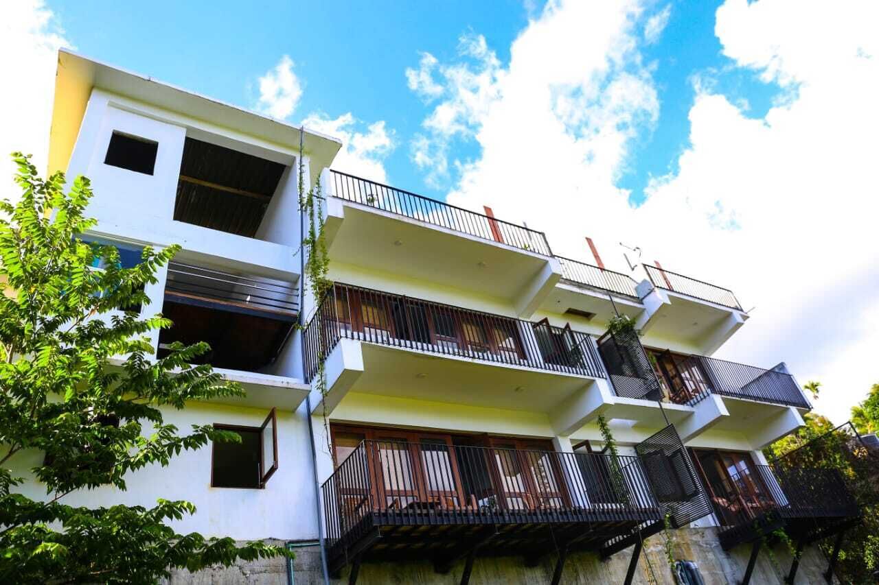 A multi-story residential building with balconies, white walls, and a clear sky.