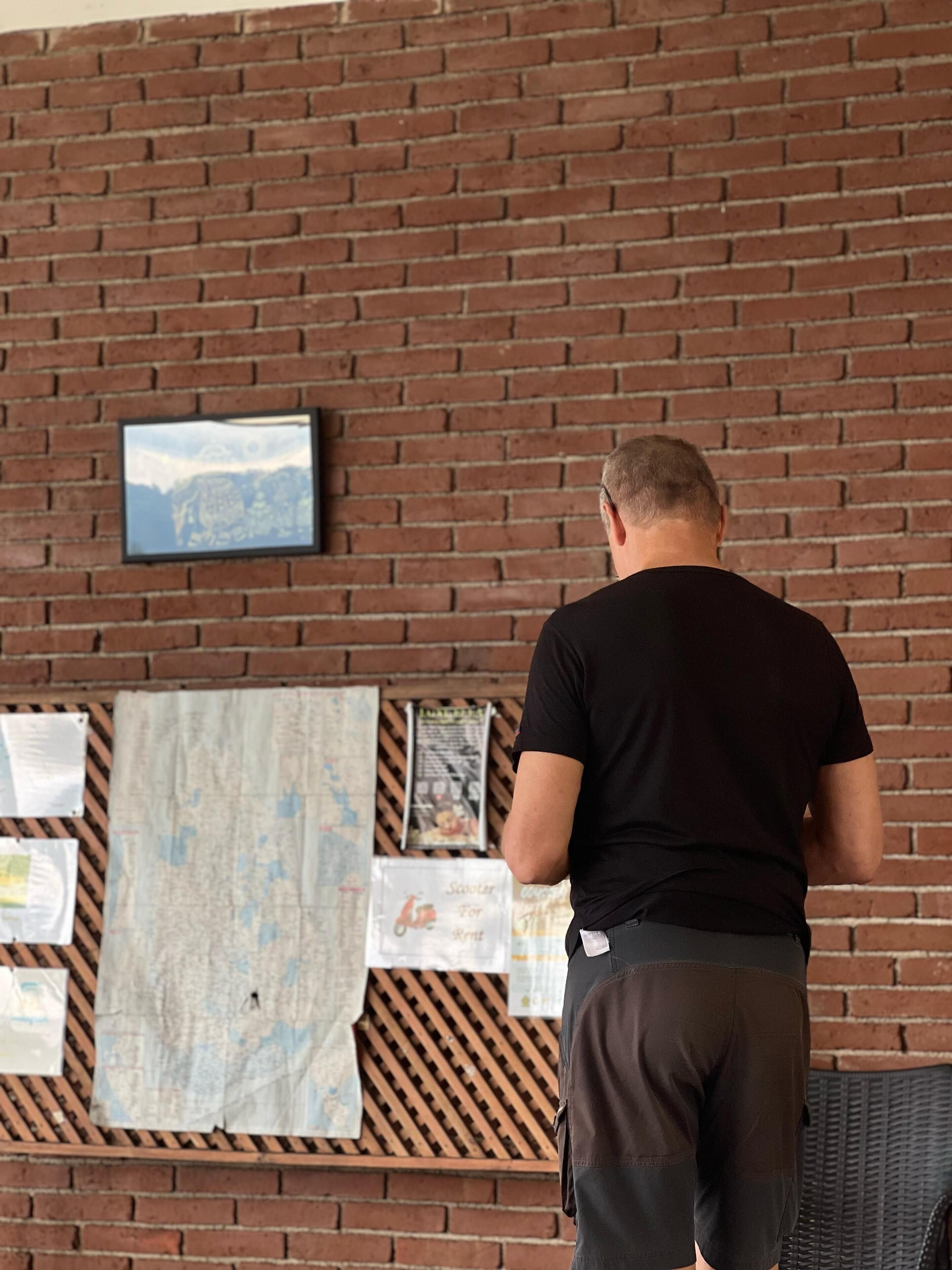 Une personne se tient devant un mur de briques, une carte et quelques feuilles de papier étant accrochées à ce mur.