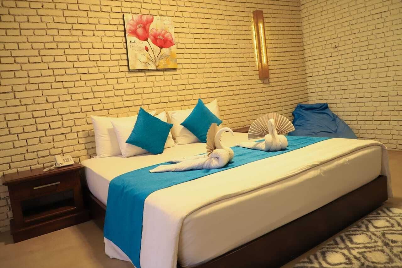 Habitación de hotel con pared de ladrillo, cama con ropa de cama azul y blanca, y un cuadro de flores.