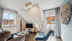 Ein modernes Wohnzimmer mit Fernseher, Sitzgelegenheiten und einem großen Fenster.