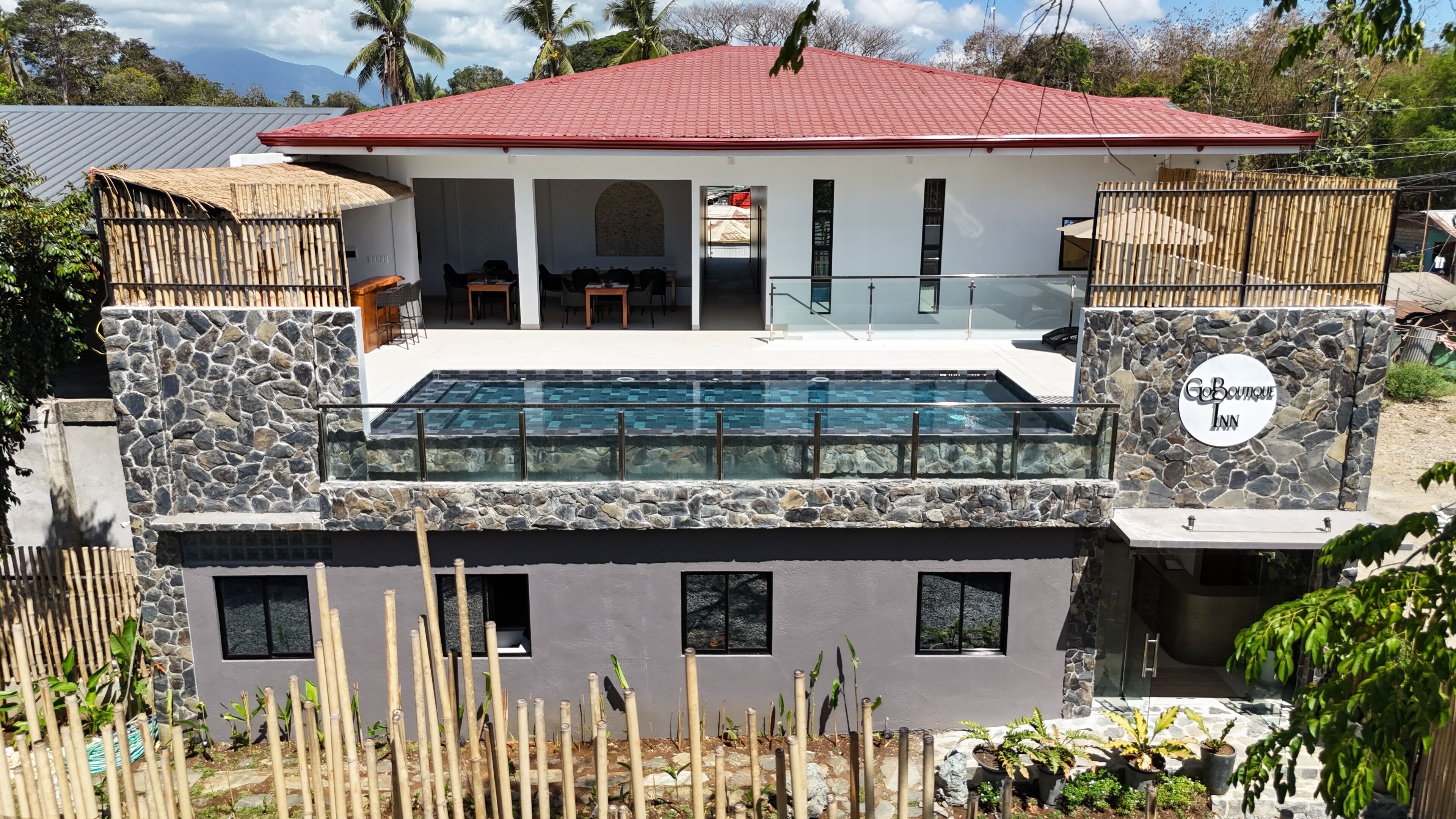 A two-story building with a swimming pool, stone walls, and a red roof.