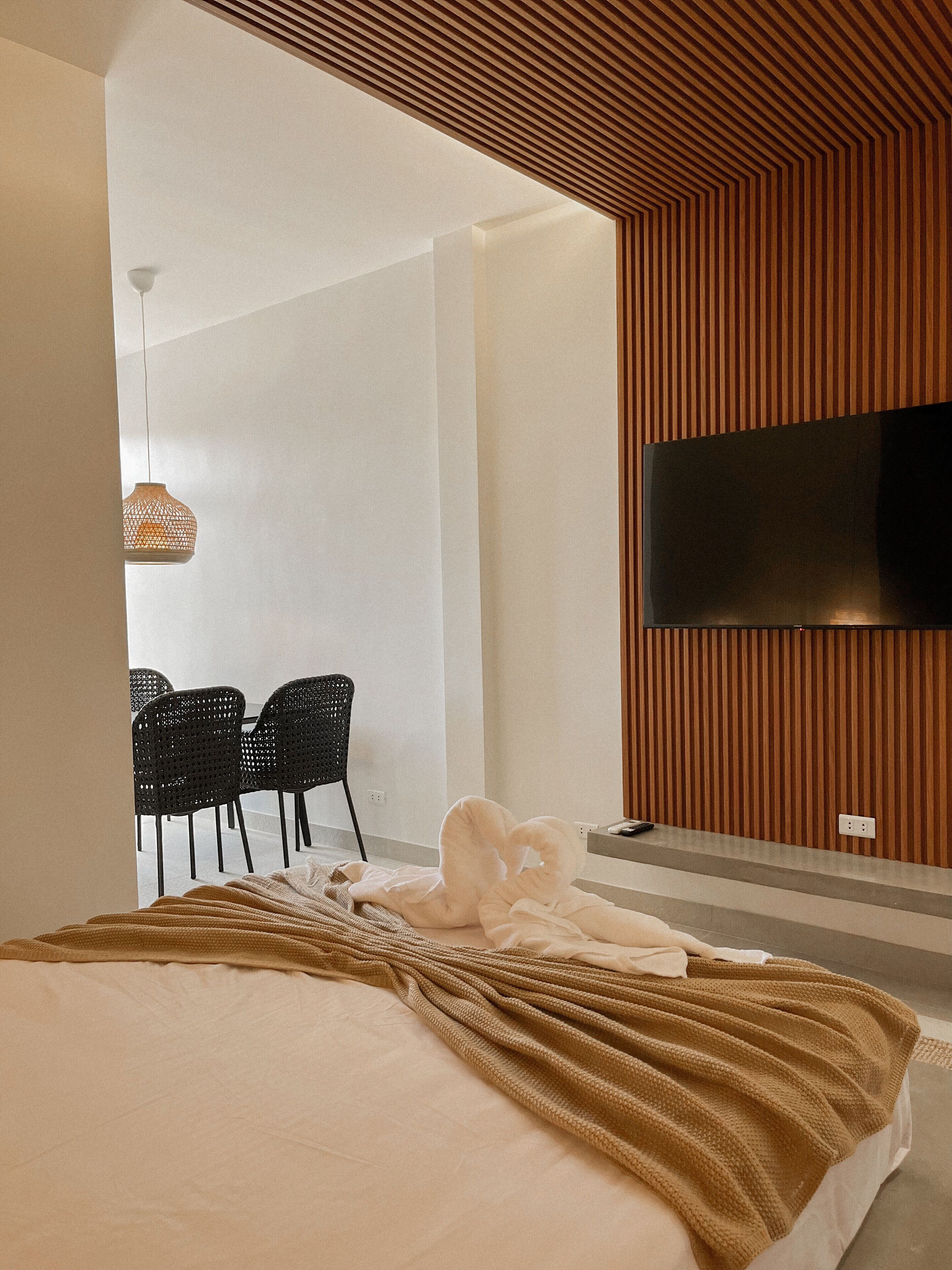 A modern hotel room with a large bed, a flat-screen TV mounted on the wall, and a seating area with chairs.