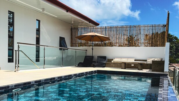 Una piscina con borde de azulejos, barandilla de vidrio y cerca de madera.