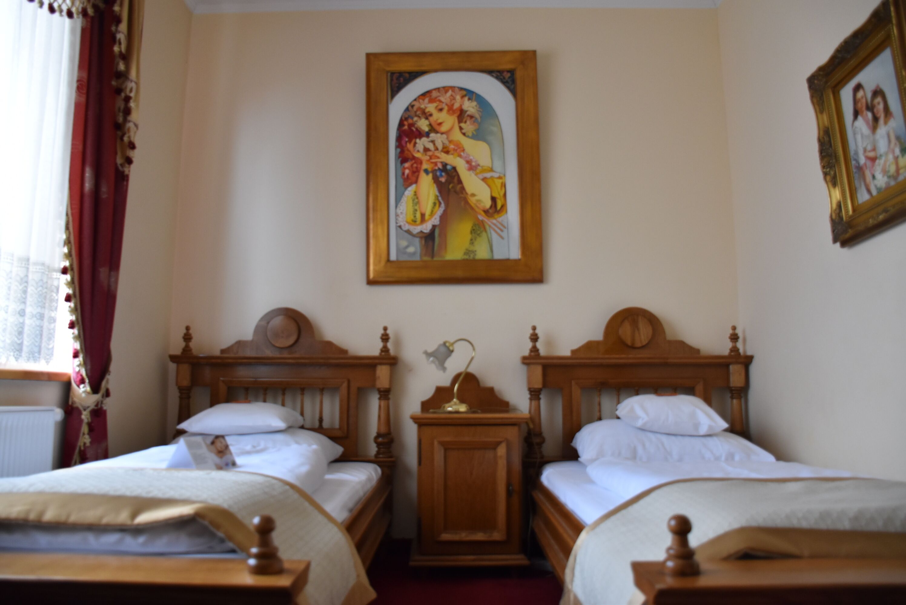 Een hotelkamer met twee houten bedden, een nachtkastje met een lamp, en een lijst met een foto aan de muur.