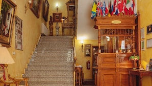 A grand staircase leading to a reception area with multiple flags, framed artwork, and traditional decor. - Hotel Grande (Celje)