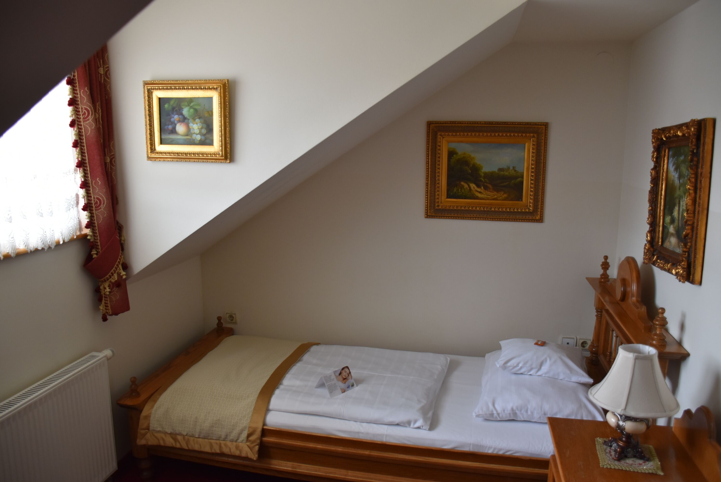 A bedroom with a single bed, a wooden headboard, a bedside table with a lamp, and two framed pictures on the wall.