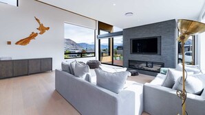 Un salon moderne avec un canapé d’angle gris, un téléviseur à écran plat et une grande fenêtre donnant sur un paysage montagneux.