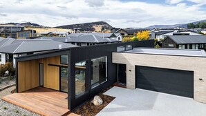 Une maison moderne avec un garage, une terrasse en bois et une vue sur la montagne.