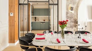 A dining area with a marble table set for six, a vase of red roses, and a modern kitchen in the background.