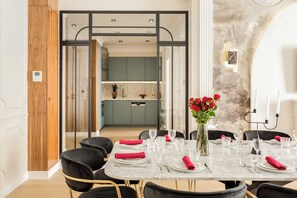 Comedor con una mesa de mármol dispuesta para seis personas, un jarrón de rosas rojas y una cocina moderna al fondo.