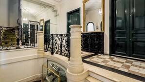 A grand staircase with ornate black railings, a checkered floor, and a large mirror with an ornate frame.