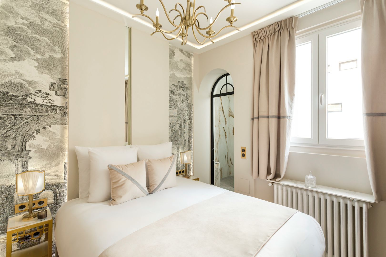 A bedroom with a large bed, a chandelier, a mirror, and a window with curtains.