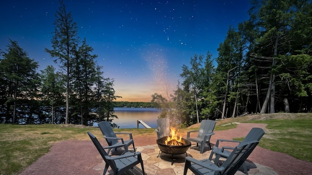 A fire pit with chairs, a stone patio, and a lake view at dusk.