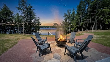 Un foyer avec des chaises, une terrasse en pierre et une vue sur le lac au crépuscule.