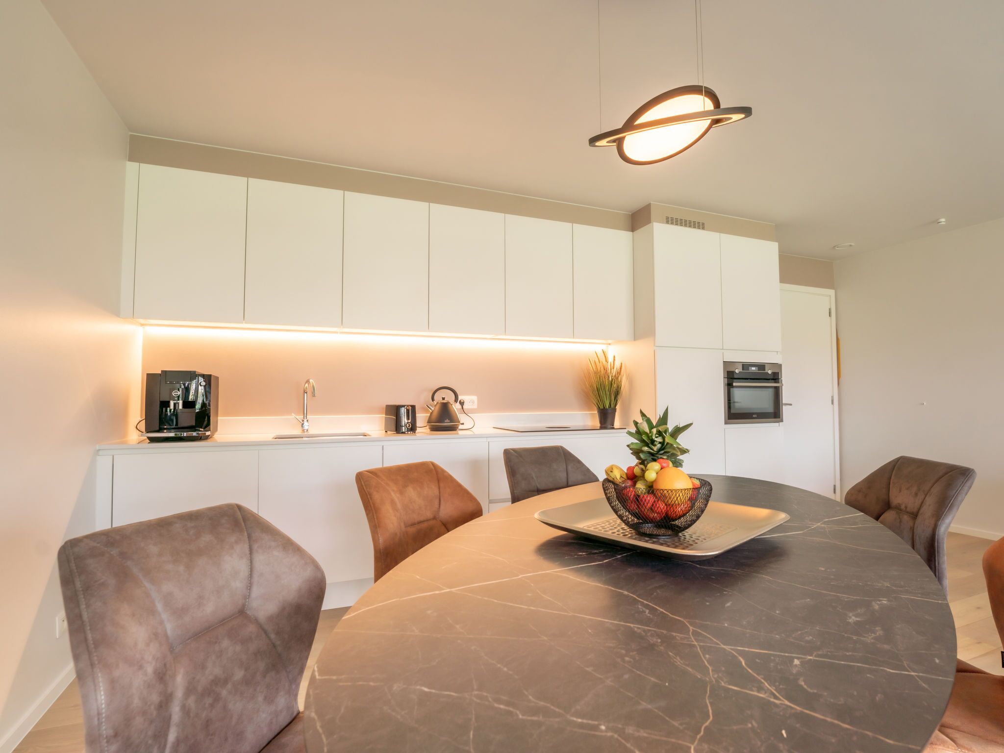 Een moderne keuken met witte kasten, een ingebouwde oven en een koffieapparaat.