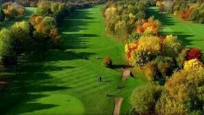 Um campo de golfe com um green bem cuidado, árvores com folhagem de outono e um céu limpo.