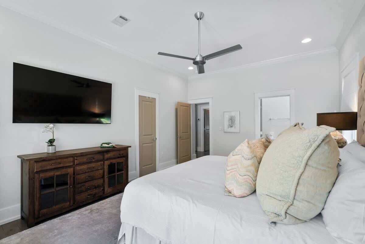 A bedroom with a bed, a television mounted on the wall, a ceiling fan, and a wooden dresser.