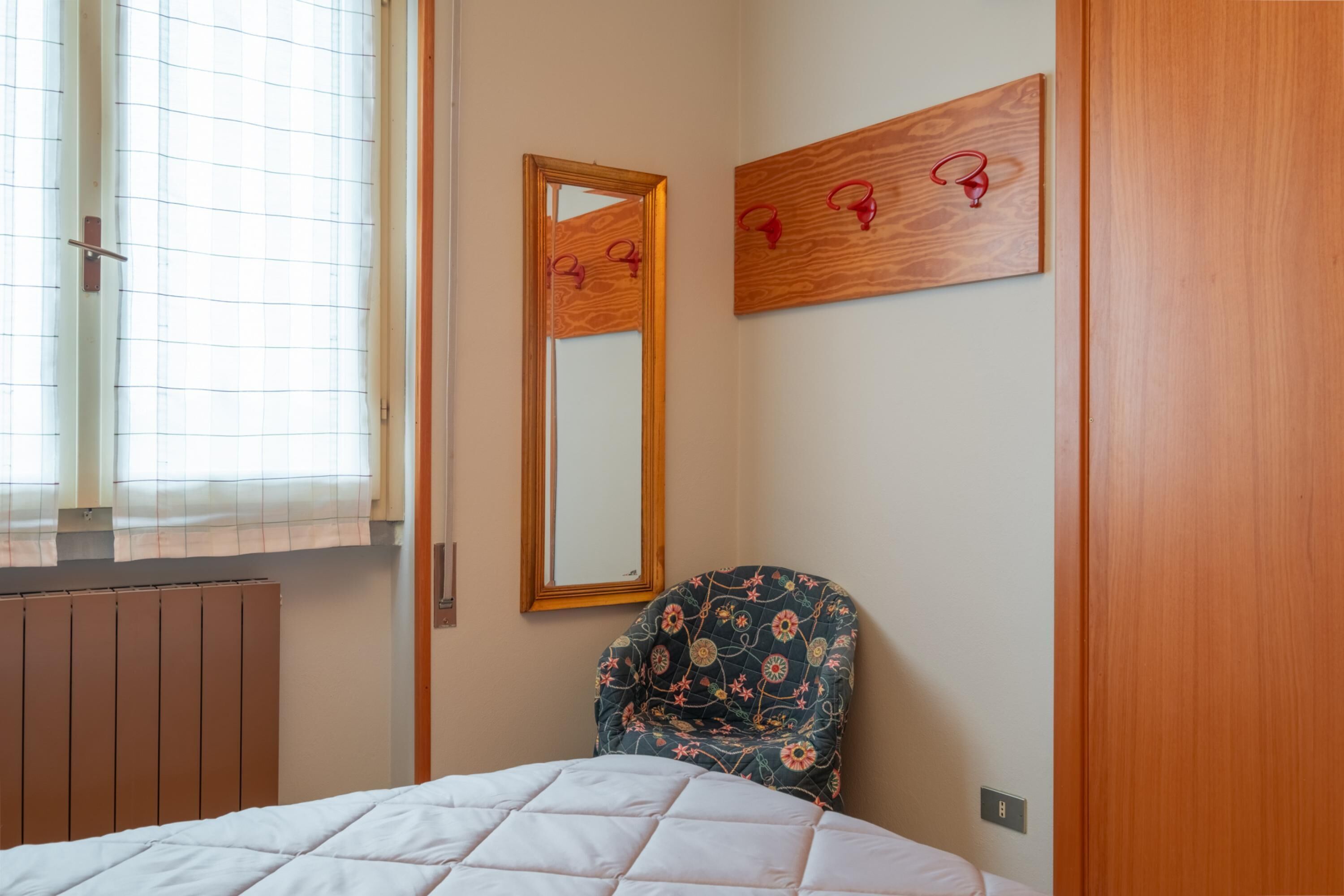 A bedroom with a bed, a chair, a mirror, and a radiator.