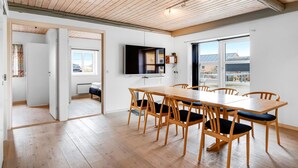 A spacious dining area with a long wooden table and chairs, a flat-screen TV mounted on the wall, and large windows offering a view of the outdoors. - "Nafne" - 1.2km from the sea by Interhome (Hvide Sande)