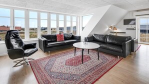 A spacious living room with a large window, a black leather sofa, a coffee table, and a patterned rug. - "Nafne" - 1.2km from the sea by Interhome (Hvide Sande)