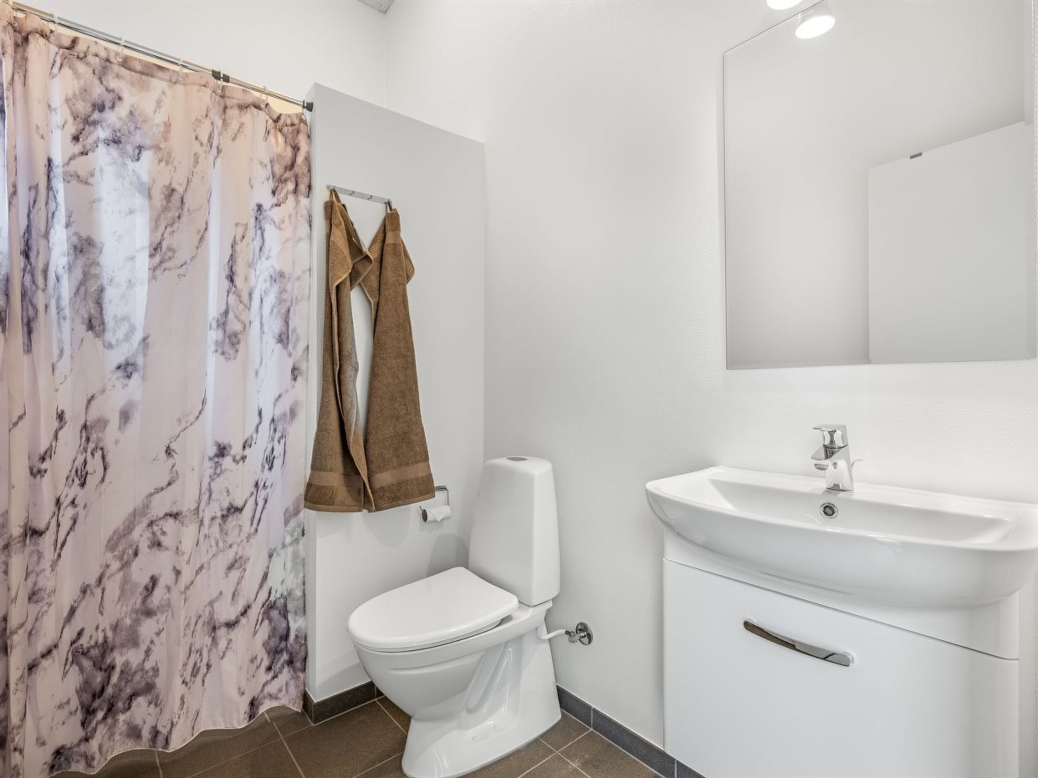 A bathroom with a toilet, sink, and marble-patterned shower curtain.