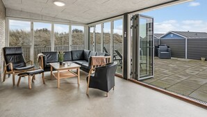 A spacious patio area with a black leather sofa, wooden chairs, and a small table.