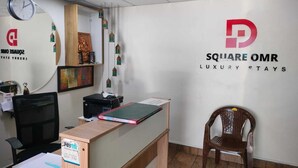 Ein Empfangsschalter mit einer Uhr, gerahmten Kunstwerken und einem Schild mit der Aufschrift 'Square OMR Luxury Stays'.