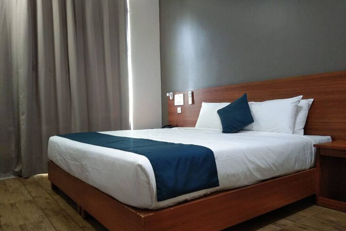 A hotel room with a wooden bed, white and blue bedding, a wooden nightstand, and a grey wall.
