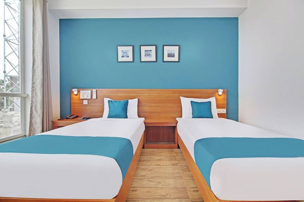 A hotel room with two beds, a wooden headboard, a window with a view, and three framed pictures on the wall.