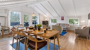 Ein großzügiger Wohnbereich mit hoher Decke, Holzboden, einem Esstisch mit Stühlen, einer Couch und einem Fernseher.