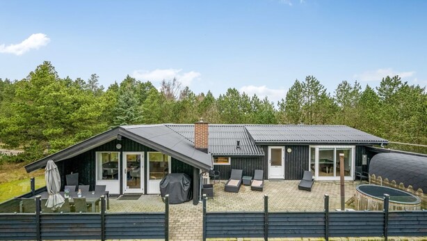Ein modernes Haus mit einer Terrassenfläche, Sitzgelegenheiten im Freien und einem überdachten Grillbereich.