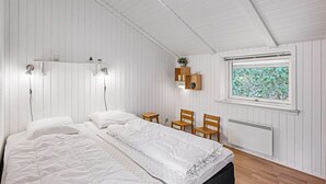 Ein Schlafzimmer mit einem Bett, zwei Stühlen, einem Fenster mit Blick auf Bäume und einer Heizung.