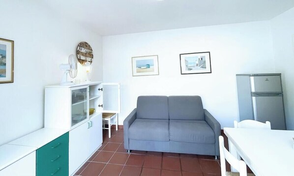 A compact kitchen with a grey sofa, white cabinets, a small table, and a refrigerator.