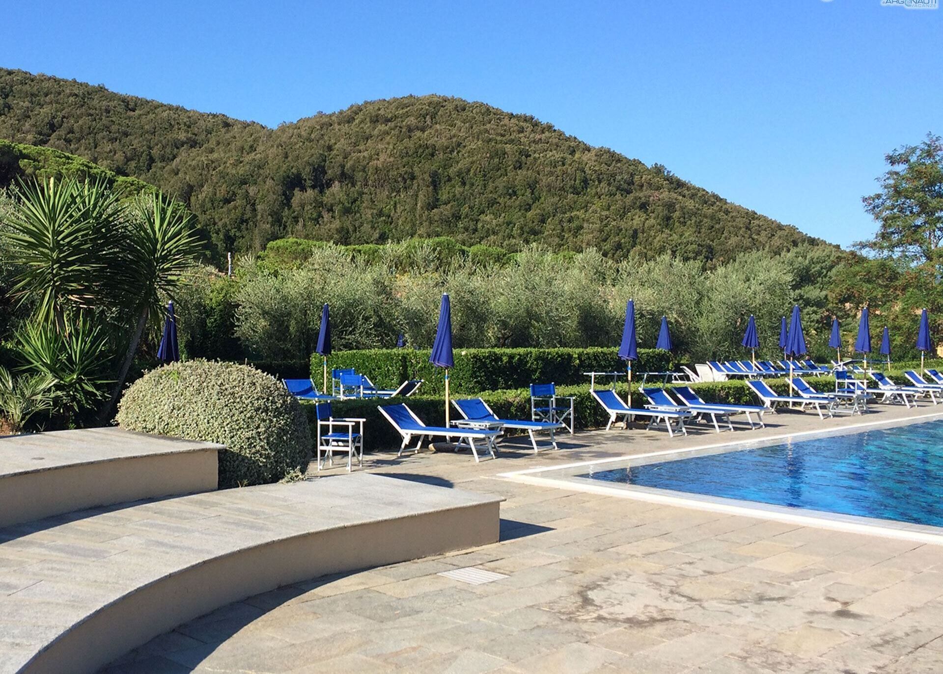 A poolside area with lounge chairs and umbrellas, surrounded by greenery and hills.