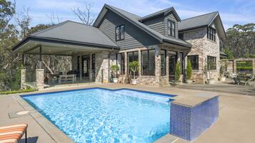 A two-story house with a swimming pool, stone exterior, and large windows.