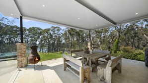 An outdoor patio with a wooden table and benches, a brick chimney, and a view of trees. - Bellmohr House on the Lake (Wentworth Falls)