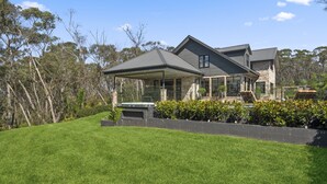 A modern house with a covered patio, stone exterior, and lush green lawn. - Bellmohr House on the Lake (Wentworth Falls)