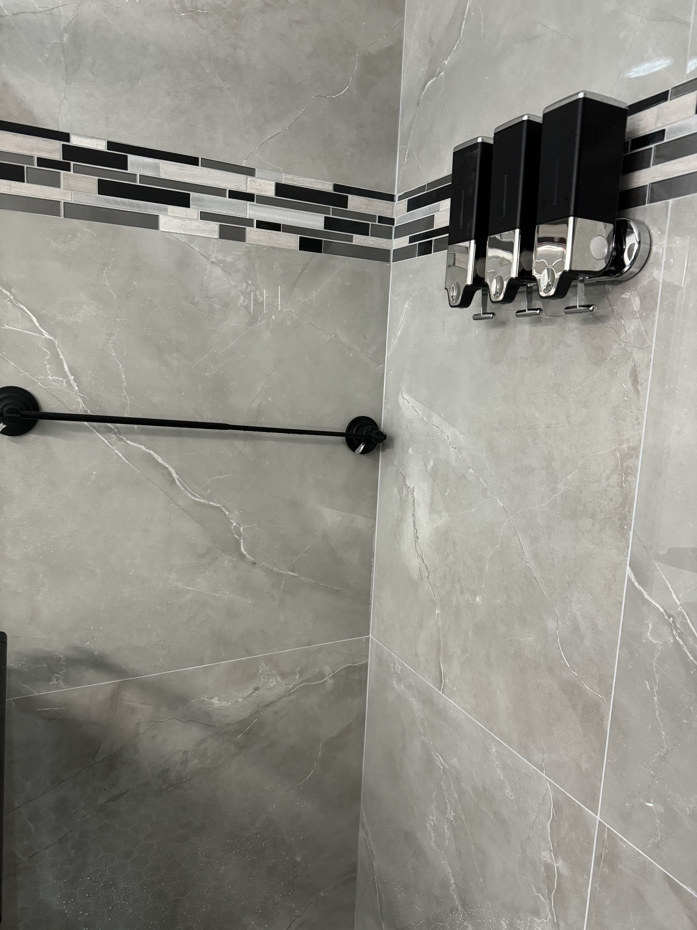 Un baño con baldosas de mármol gris, un perchero para toallas y un dispensador de jabón negro.
