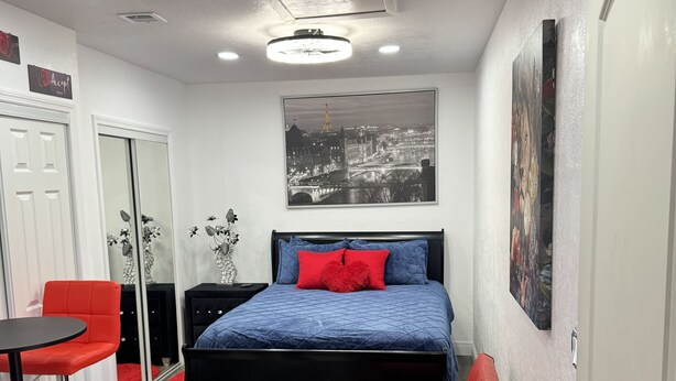 A compact room with a bed, a red sofa, a small round table, and a chair.