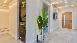 Un pasillo moderno con lavadora, una planta grande en maceta y una puerta de madera.