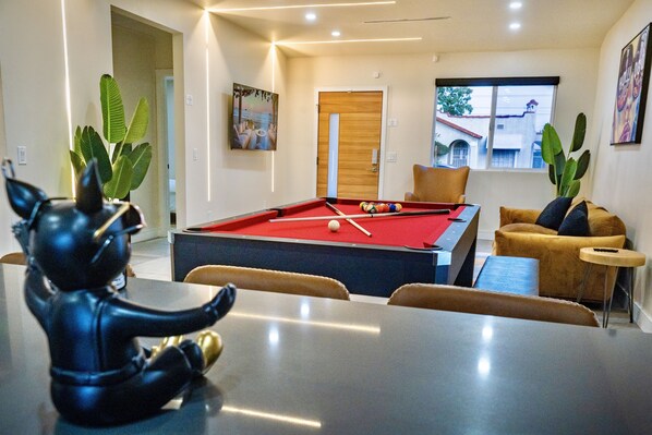 Ein modernes Zimmer mit Pooltisch, bequemen Sitzgelegenheiten und großen Fenstern.
