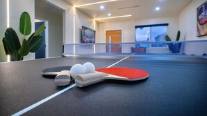 Una mesa de ping pong con pelotas y paletas, una planta y una puerta en una habitación moderna con vistas.
